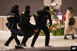 Полицейские задерживают мужчину возле мемориала жертвам политических репрессий, куда жители Санкт-Петербурга несут цветы, свечи и фотографии в память об Алексее Навальном. 16 февраля 2024 года. Фото: AP
