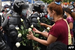 Протестующие вставляют цветы в щиты полицейских во время протестов в Янгоне 6 февраля