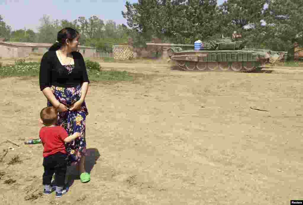 Женщина с ребенком наблюдает за передвижением военной техники через поселок. Конвой едет в Кузьминский - тренировочную военную базу на границе России и Украины, 26 мая 2015