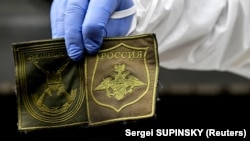 Украинский судебно-медицинский эксперт показывает нашивки с формы убитого российского солдата, эксгумированного в селе Заваливка к западу от Киева, 11 мая 2022 года