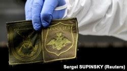 Украинский криминалист показывает нашивки, найденные на теле российского солдата, эксгумированного в селе Заваловка Киевской области, 11 мая 2022 года