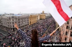 A woman waves the former Belarusian national flag from a rooftop as Belarusian protesters march to Minsk's Independence Square on August 23, 2020.