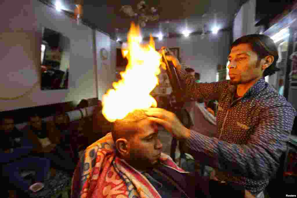 Палестинский парикмахер Рамадан Одван причесывает и выравнивает волосы клиента с помощью огня в салоне города Рафах в Секторе Газа&nbsp;(Reuters/Ibraheem Abu Mustafa)