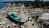 INDONESIA -- People drive past a washed up boat and collapsed buildings in Palu on October 1, 2018, after an earthquake and tsunami hit the area on September 28.