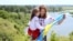 UKRAINE – Happy smiling Ukrainian Mom and daughter in vyshyvanka (embroidered shirts) with a yellow-blue flag on a background of mountains and a river