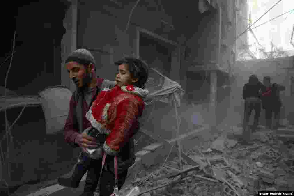 Мужчина выносит ребенка из-под завалов после авиаударов в городе Дума в Сирии. 7 февраля