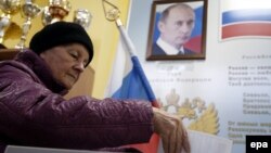 An elderly woman casts her ballot in front of a portrait of Russian President Vladimir Putin at a polling station in a Moscow public school during Russia's 2016 parliamentary elections.