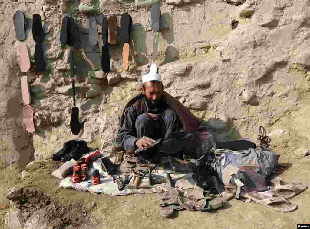 Сапожник начищает ботинки клиента, сидя на обочине в Кабуле. ​(Reuters/Omar Sobhani)