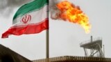 A gas flare on an oil production platform in the Soroush oil fields is seen alongside an Iranian flag in the Persian Gulf, Iran, July 25, 2005. 