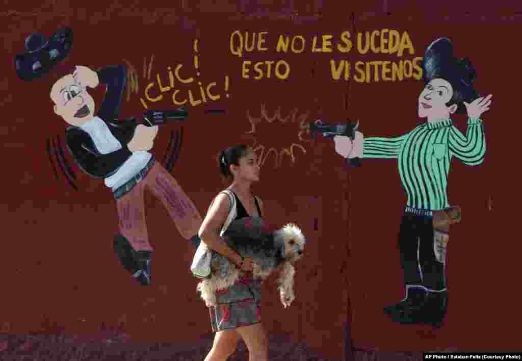 Женщина с собакой в руках проходит мимо оружейной лавки в Сан-Педро-Сула, Гондурас. Этот город &ndash; одно из самых криминальных мест мира. Здесь разрешено огнестрельное оружие и процветают наркокартели. Нередко жители становятся жертвами перестрелок между группировками. Март 2012