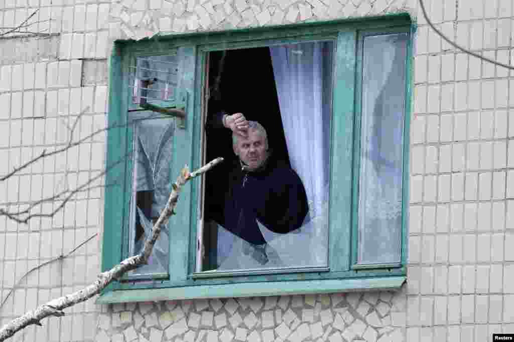 Житель Краматорска выглядывает из окна, разбитого в результате обстрела города 10 февраля