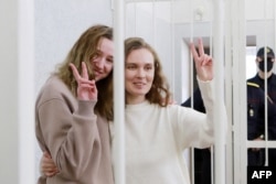 Belsat TV journalists Katsyaryna Andreyeva and Daria Chultsova, who were detained in November while reporting on anti-government protests, flash the V-sign from a defendant's cage during their trial in Minsk on February 18, 2021.