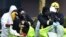 U.K. -- Members of the fire brigade are helped out of their green biohazard suits by colleagues in white protective coveralls after an operation to re-attach the tent over the bench where a man and a woman were found in critical condition sparking a major