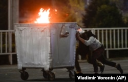 Protesters push a burning trash can toward riot police during an October 5, 2020 rally in Bishkek against the preliminary results of Kyrgyzstan's parliamentary elections.
