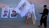 AFGHANISTAN - A vendor holds a Taliban flag next to the posters of Taliban leaders Mullah Abdul Ghani Baradar and Amir Khan Muttaqi (L) as he waits for customers along a street in Kabul on August 27, 2021