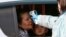 Kazakhstan - A medic wearing a protective gear checks the temperature of a woman at a checkpoint on the outskirts of Almaty on March 19, 2020, after authorities locked down the city to contain the spread of the COVID-19 coronavirus. (Photo by Ruslan PRYAN