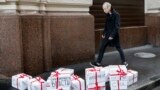RUSSIA -- An opposition activist wearing a rubber mask depicting Russian President Vladimir Putin walks past gift boxes with letterings reading "trial", "resignation", "impeachment", "true election", "lustration" and others during an event dedicated to P