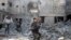 SYRIA -- A man carries an injured boy as he walks on rubble of damaged buildings in the rebel held besieged town of Hamouriyeh, eastern Ghouta, near Damascus, February 21, 2018