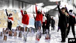 Wearing protesters' symbolic colors of red and white, feminist activists take part in a February 14, 2021 flash mob in Minsk against police violence. On display are photographs of women imprisoned in connection with protests over Belarus' August 9, 2020 presidential elections .