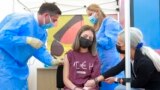 ROMANIA -- Romanian girl Cezara Marina (C), 13, is watched by her mother Alina (R) as she is about to get her first vaccine dose from the head of the Romanian Anti-COVID Vaccination Authority, military doctor Valeriu Gheorghita (L), at a Covid-19 Childr