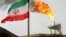 A gas flare on an oil production platform in the Soroush oil fields is seen alongside an Iranian flag in the Persian Gulf, Iran, July 25, 2005. 