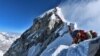 heavy traffic of mountain climbers lining up to stand at the summit of Mount Everest