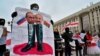 UKRAINE -- A member of the Belarus diaspora holds a placard depicting Belarusian President Aleksander Lukashenko (R) and Russian President Vladimir Putin during a rally supporting Internatioanl Solidarity Day With Belarus in the center of Kyiv, February 