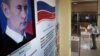 RUSSIA -- A man wearing a protective face mask and gloves prepares to cast his ballot during early voting in a referendum on amendments to the Russian Constitution next to a portrait of Russian President Vladimir Putin at a polling station in Moscow, June