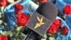 Kazakhstan – people are laying flowers to the Independence Monument in Almaty. Azattyq logo / label