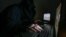 A man in a hood types on two laptop computer