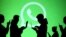 Silhouettes of laptop and mobile device users are seen next to a screen projection of Whatsapp logo in this picture illustration