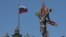 RUSSIA -- A rainbow colour ribbon tied to a crucifix is seen next to a Russian flag fluttering atop the State Hermitage Museum during the LGBT (lesbian, gay, bisexual, and transgender) community rally in central St. Petersburg, August 4, 2018