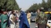Силы "Талибана" блокируют дорогу около аэропорта, пока рядом проходит женщина, 27 августа 2021 года