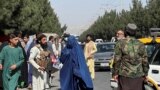 Силы "Талибана" блокируют дорогу около аэропорта, пока рядом проходит женщина, 27 августа 2021 года
